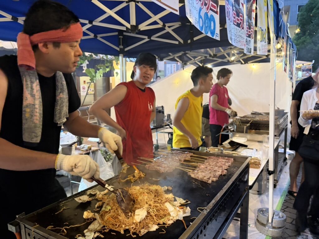 夕方の屋台で焼きそばと牛串を調理するスタッフ